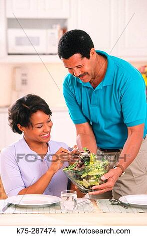 Picture - Husband serves salad to wife. Fotosearch