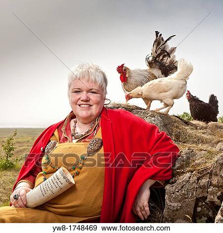 Stock Photo - Icelandic Female priest on her farm with chickens, Hvalfjordur, Iceland Dressed in traditional viking clothing and holding a bull horn In Icelandic referred to as practicing? sa beliefs or Paganism. Fotosearch