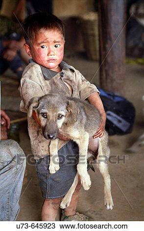 Stock Image - In a small Yi minority village this small boy holds his pet dog.. Fotosearch