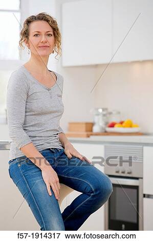 Stock Photo - Independent young woman sitting her kitchen. Fotosearch