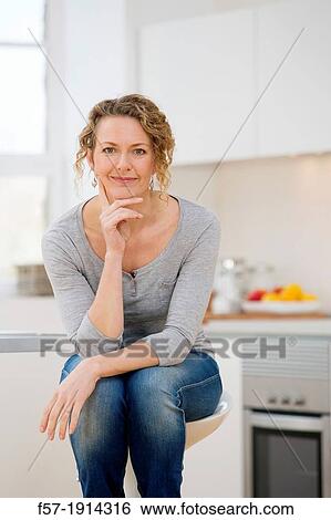 Stock Photograph - Independent young woman sitting her kitchen. Fotosearch