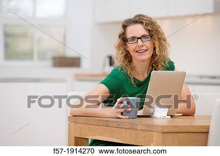 Stock Image - Independent young woman working at home on a tablet computer. Fotosearch