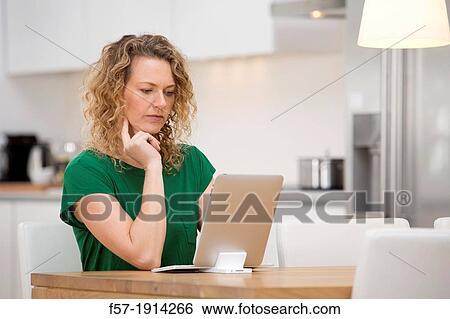 Independent young woman working at home on a tablet computer View Large Photo Image Stock Photograph - Independent young woman working at home on a tablet computer. Fotosearch