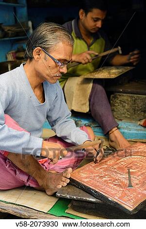 Stock Image - India, Uttar Pradesh, Varanasi, Craftsmen embossing copper plates.. Fotosearch