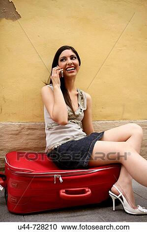 Stock Image - Indian woman traveling an talking with a red suitcase. Fotosearch