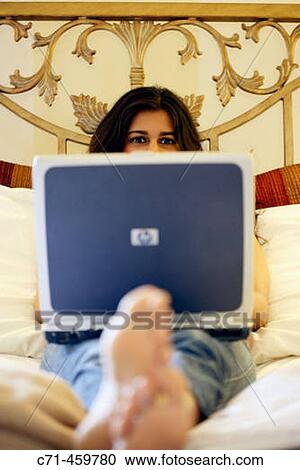 Stock Image - Indian woman working on laptop in bed. Fotosearch