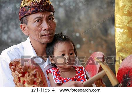 Stock Image - Indonesia, Bali, Mas, temple festival, people, odalan, Kuningan holiday, gamelan musician with daughter,. Fotosearch