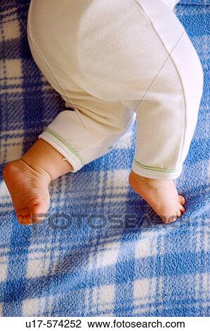 Stock Image - Infant's legs and feet pushing against blue plaid fleece blanket.. Fotosearch