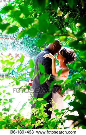 intimate garden wedding and reception with an interracial bride & groom finding privacy for a passionate moment alone by a water fountain View Large Photo Image Stock Photo - intimate garden wedding and reception with an interracial bride & groom finding privacy for a passionate moment alone by a water fountain. Fotosearch