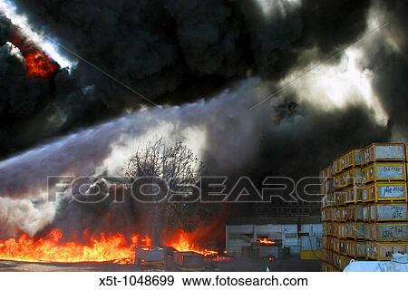 Stock Photo - Israel, Galilee, a raging wild fire in an agricultural packing plant A jet of water from the left is aimed at the flames. Fotosearch