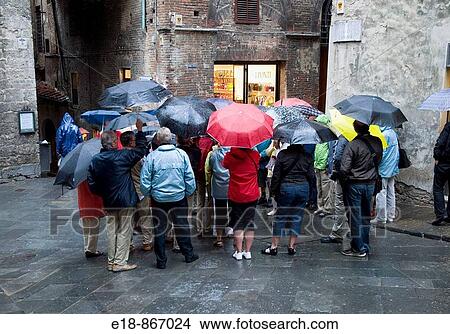 Italy, Tuscany, Siena. Group of tourists on tour of the old city on a rainy day, crowd together to hear tour guide. View Large Photo Image Picture - Italy, Tuscany, Siena. Group of tourists on tour of the old city on a rainy day, crowd together to hear tour guide.. Fotosearch