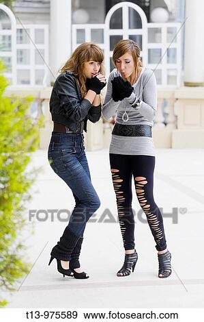 Stock Photo - It's cold here. two attractive young woman are blowing warm breath into their hands. Fotosearch