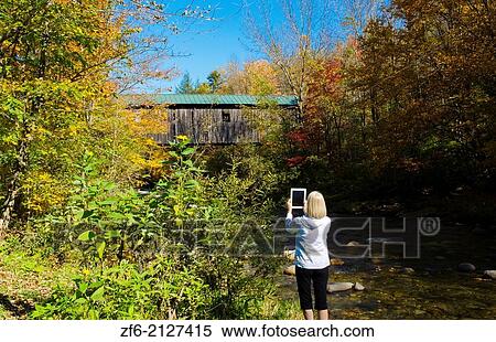 Jeffersonville Vermont covered bridge woman taking pictures with Ipad at Grist Mill Covered Bridge over river with fall foliage in Northern New England 1. View Large Photo Image Stock Photography - Jeffersonville Vermont covered bridge woman taking pictures with Ipad at Grist Mill Covered Bridge over river with fall foliage in Northern New England 1.. Fotosearch