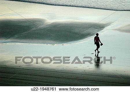 Stock Image - Jericoacoara, CearB, Brazil, a man walking along the seashore at sunset. Fotosearch