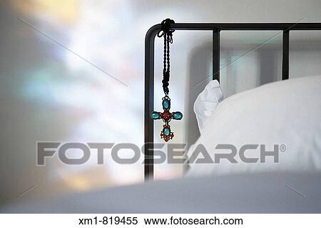 Stock Photography - Jewelled cross hanging from metal bedhead. Fotosearch