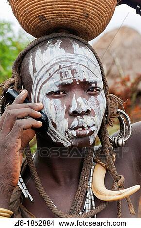 Jinka Ethiopia Africa village Lower Omo Valley Mago National Park wild tribe Mursi tribal woman with basket portrait on cell phone communicating with paint on face and traditional culture 15 View Large Photo Image Picture - Jinka Ethiopia Africa village Lower Omo Valley Mago National Park wild tribe Mursi tribal woman with basket portrait on cell phone communicating with paint on face and traditional culture 15. Fotosearch