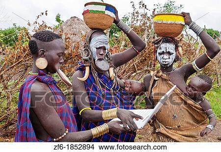 Picture - Jinka Ethiopia Africa village Lower Omo Valley Mago National Park wild tribe Mursi women with clay pots in their lips working on modern computer email in tribal portrait with paint on faces and traditional culture 15. Fotosearch