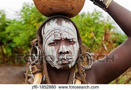 Stock Image - Jinka Ethiopia Africa village Lower Omo Valley Mago National Park wild tribe Mursi tribal woman with basket portrait with paint on face and traditional culture 15. Fotosearch