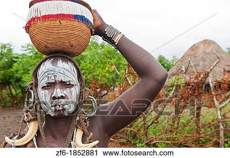 Stock Image - Jinka Ethiopia Africa village Lower Omo Valley Mago National Park wild tribe Mursi tribal woman with basket portrait with paint on face and traditional culture 15. Fotosearch