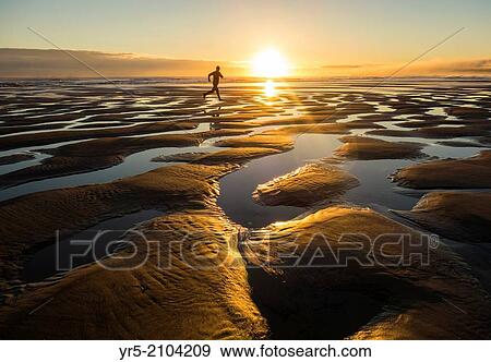Stock Photo - Jogger on beach at sunrise. Seaton Carew near Hartlepool, north east England, United Kingdom.. Fotosearch