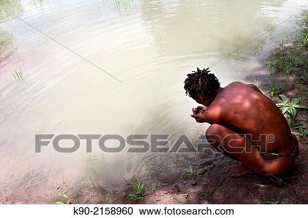 Stock Image - Ju/? hoansi San man taking water from a waterhole in the African savannah, Namibia, Africa.. Fotosearch