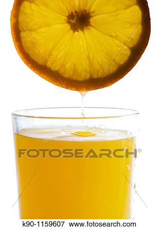 Stock Photo - Juice dropping from a slice of an orange hold above a glass filled with orange juice, white background.. Fotosearch
