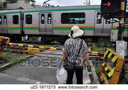 Stock Image - Kamakura, Kanagawa, Japan, a woman waiting by a grade crossing. Fotosearch