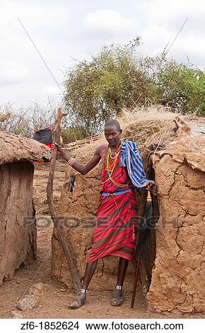 Kenya Africa Amboseli Maasai tribe village Masai man in red costume dress and beads in front of mud home in remote area of Amboseli National Park safari 1 View Large Photo Image Picture - Kenya Africa Amboseli Maasai tribe village Masai man in red costume dress and beads in front of mud home in remote area of Amboseli National Park safari 1. Fotosearch