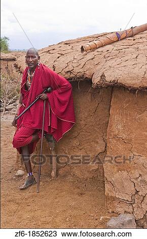Kenya Africa Amboseli Maasai tribe village Masai man in red costume dress and beads in front of mud home in remote area of Amboseli National Park safari 1 View Large Photo Image Stock Image - Kenya Africa Amboseli Maasai tribe village Masai man in red costume dress and beads in front of mud home in remote area of Amboseli National Park safari 1. Fotosearch