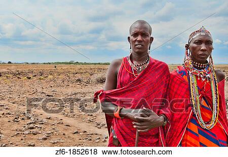 Stock Photo - Kenya Africa Amboseli Masai man and woman in red costume dress and beads in Amboseli National Park safari out alone in jungle 1. Fotosearch