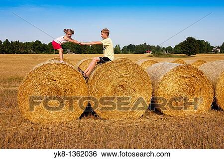 Stock Photograph - Kids Playing on Corn Bales Holding Hands, Estonia. Fotosearch