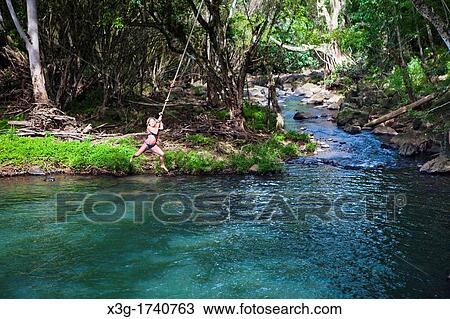 Stock Image - Kipu Falls is a secret swimming hole on Hawaii's island of Kauai, USA. A gigantic rope swing allows for thrill seekers to swing off the cliff and into the water.. Fotosearch