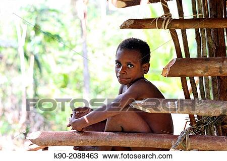 Stock Image - Kombai boy sitting in front of a wooden house, Papua, Indonesia, Southeast Asia.. Fotosearch