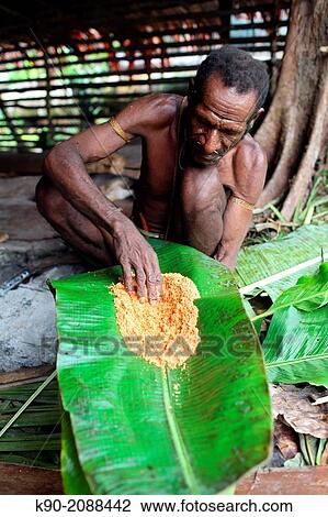 Stock Image - Kombai man making sago bread, wearing a necklace made of dog teeth, Papua, Indonesia, Southeast Asia.. Fotosearch