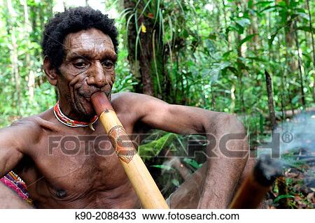 Stock Image - Kombai man smoking a pipe in the jungle, Papua, Indonesia, Southeast Asia.. Fotosearch
