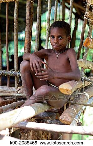 Stock Photography - Kombai sitting in front of a wooden house, Papua, Indonesia, Southeast Asia.. Fotosearch
