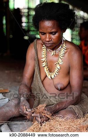 Stock Photo - Kombai woman sitting with necklace made of dog teeth, knitting a dress made of palm tree fibre, Papua, Indonesia, Southeast Asia.. Fotosearch