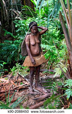 Stock Image - Kombai woman standing in jungle with necklace made of dog teeth and traditional palm leave dress, Papua, Indonesia, Southeast Asia.. Fotosearch
