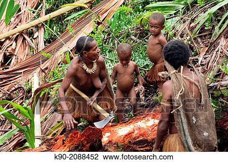 Stock Image - Kombai woman with kids, cutting a Sago palm tree, Papua, Indonesia, Southeast Asia.. Fotosearch
