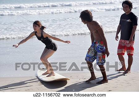 Stock Image - Kuta Beach (Bali, Indonesia): a Japanese tourist learning to surf on the shore. Fotosearch
