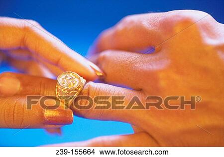 Picture - Lady slipping ring on male finger.. Fotosearch