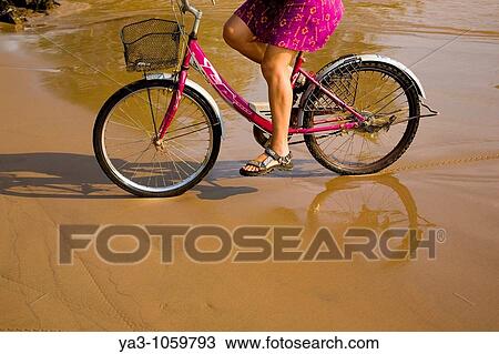 Stock Image - Laos, Si Phan Don Four Thousand Islands, Don Khon Female tourist on a hired bicycle on a sandy beach on the island of Don Knon. Fotosearch