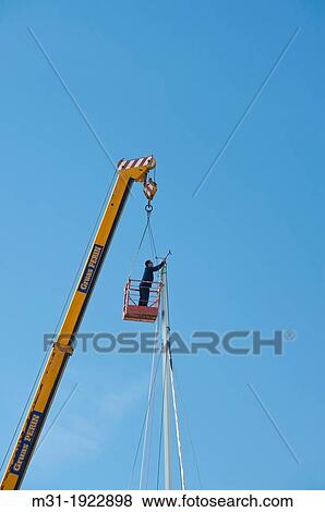 Stock Photo - Large industrial mobile crane and worker fixing a mast of a sailboat, Cartagena port, Cartagena, Murcia region, Spain, Europe. Fotosearch