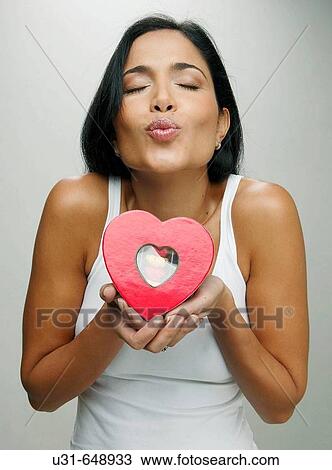 Stock Image - Latin girl blowing a kiss giving a valentine's chocolate heart. Fotosearch