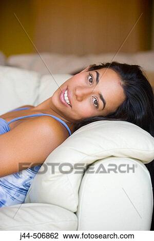 Stock Image - Latin woman resting on couch smiling. Fotosearch