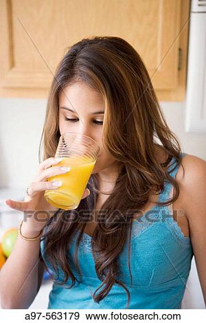 Latina teen girl in blue top drinking a glass of orange juice while standing in kitchen. View Large Photo Image Stock Photo - Latina teen girl in blue top drinking a glass of orange juice while standing in kitchen.. Fotosearch