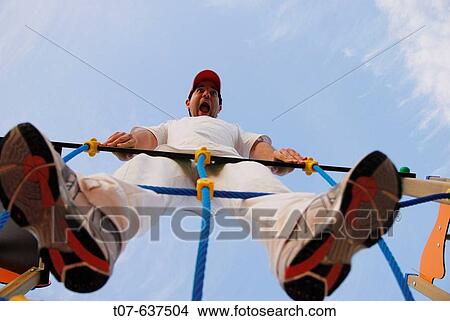Picture - Latino man holding onto playground ropes.. Fotosearch