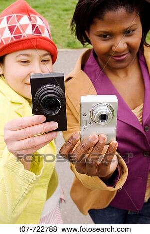 Stock Photo - Latino woman and Afro-American woman holding digital cameras.. Fotosearch