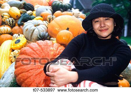 Stock Photo - Latino woman sitting next to Pumpkins. Pumpkins are synonymous with autumn, Thanksgiving and Halloween in the United States.. Fotosearch