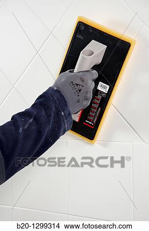 Picture - Laying tiles, glue mortar, using grout float, new homes under construction, construction site. Fotosearch